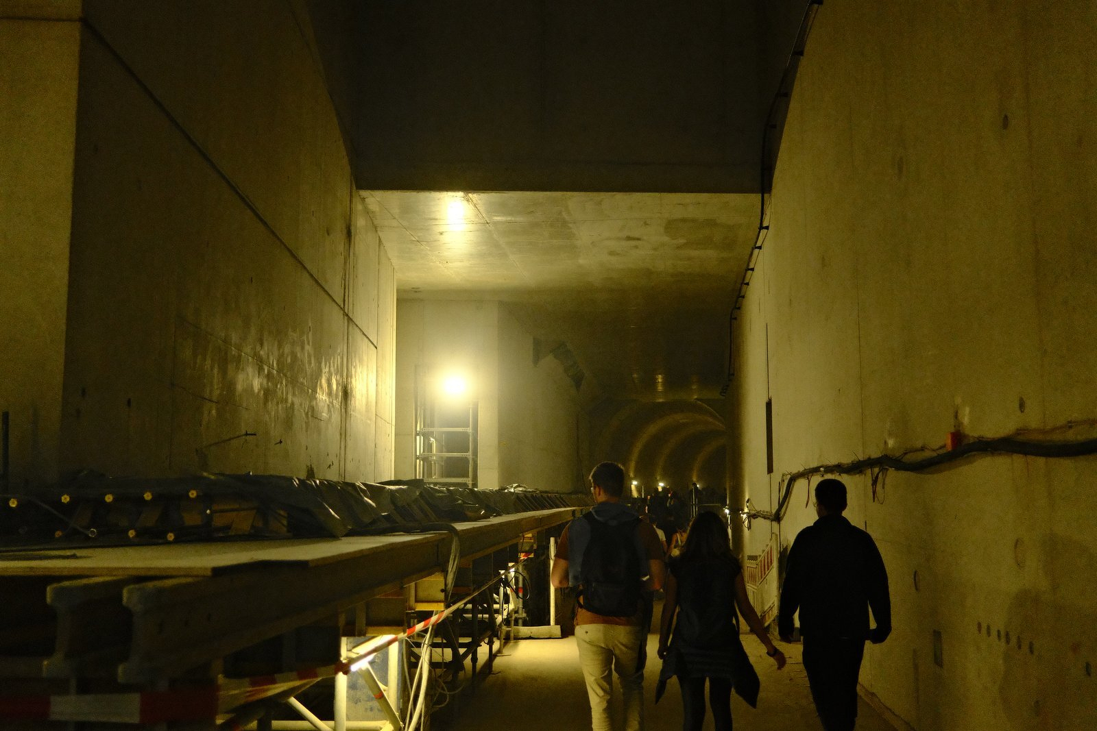 Visitors walking along a tall concrete wall in the station hall